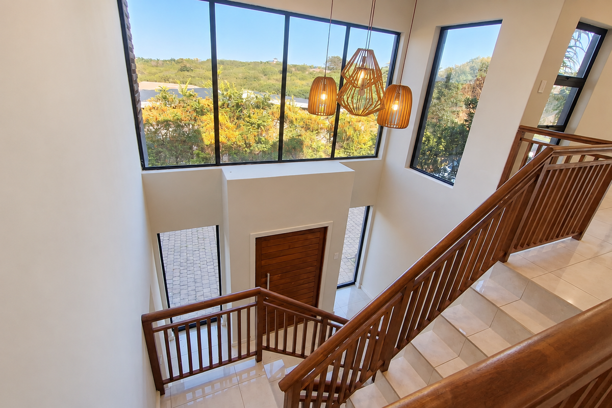 Spacious double-volume entrance hall featuring a grand wooden staircase, large windows providing abundant natural light, and high-quality tiled flooring.