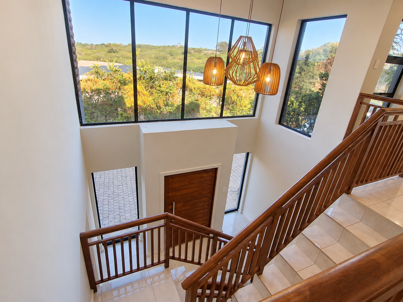 Spacious double-volume entrance hall featuring a grand wooden staircase, large windows providing abundant natural light, and high-quality tiled flooring.