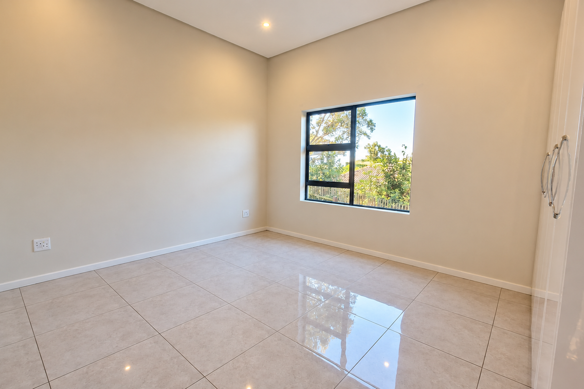 A bright, empty bedroom featuring neutral tiled flooring, built-in cupboards, and a large window providing natural light.