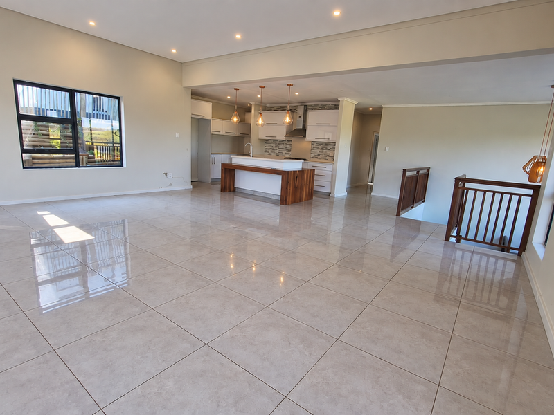 Spacious open-plan living area featuring large porcelain floor tiles, a modern kitchen with a central island, and a staircase with a wooden balustrade.