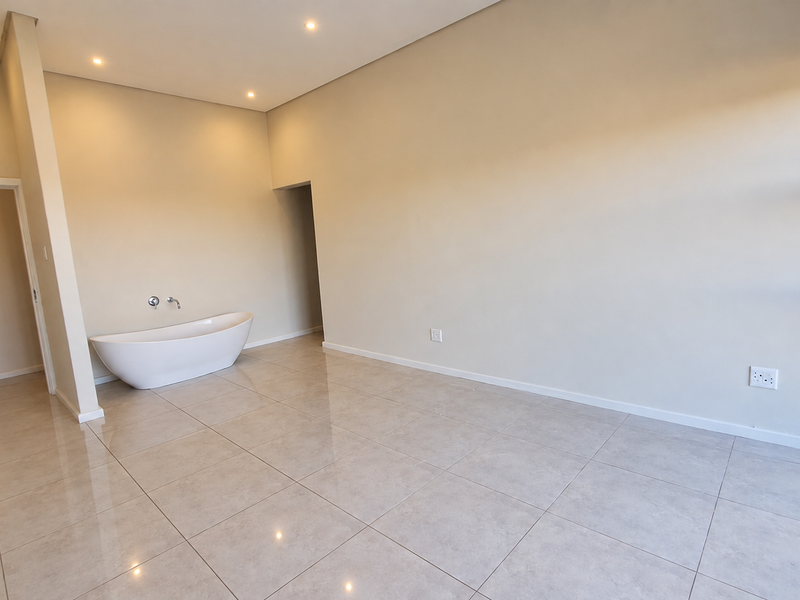 A spacious, modern bathroom featuring a sleek freestanding bathtub, neutral tiled flooring, and recessed ceiling lighting in a clean, minimalist setting.