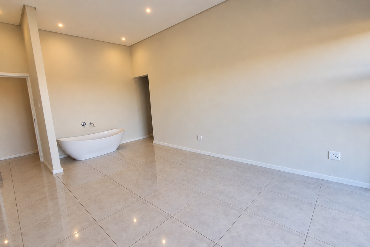 A spacious, modern bathroom featuring a sleek freestanding bathtub, neutral tiled flooring, and recessed ceiling lighting in a clean, minimalist setting.