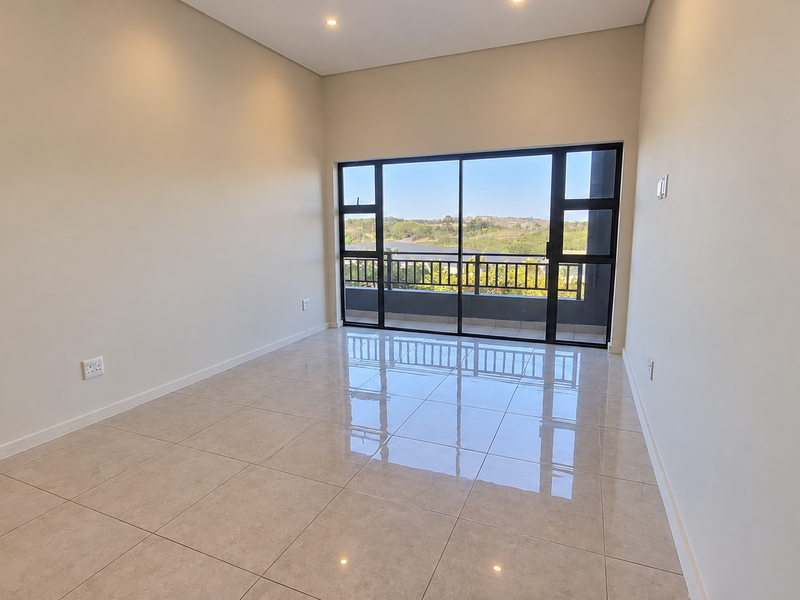 A bright, empty living room featuring polished tile flooring, recessed lighting, and large sliding glass doors that open onto a balcony with scenic views.