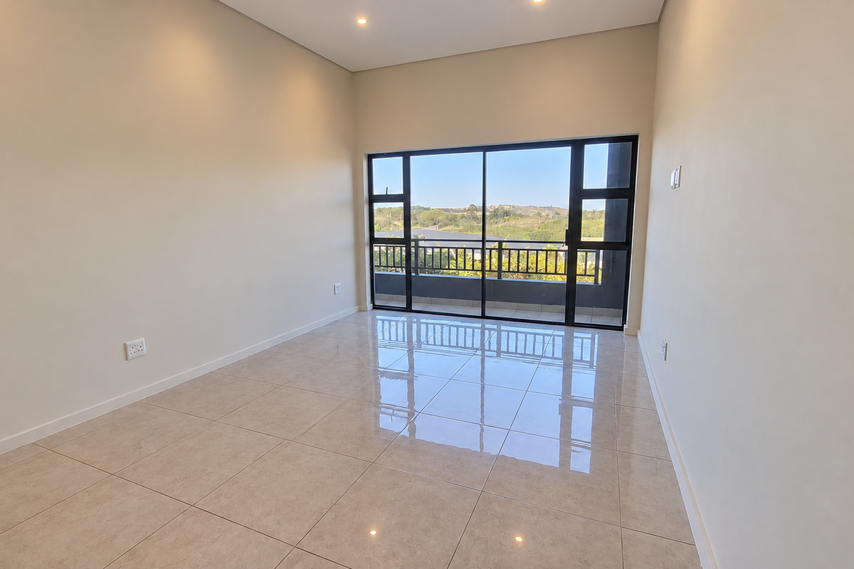 A bright, empty living room featuring polished tile flooring, recessed lighting, and large sliding glass doors that open onto a balcony with scenic views.