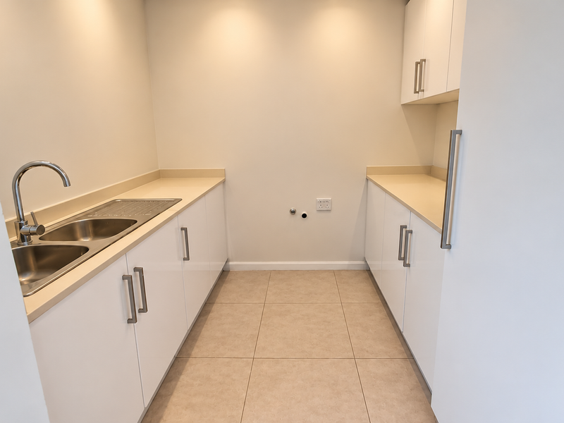 A clean, modern laundry room featuring white built-in cabinetry, stone countertops, a stainless steel sink, and dedicated plumbing connections for appliances.