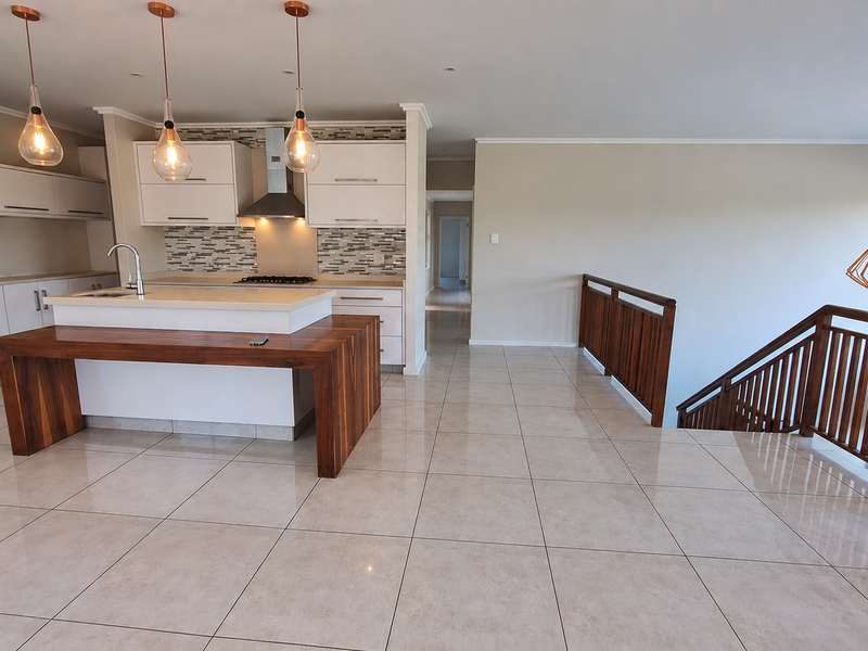 Spacious open-plan kitchen featuring a central island, modern cabinetry, tiled flooring, and a wooden staircase railing overlooking the lower level.