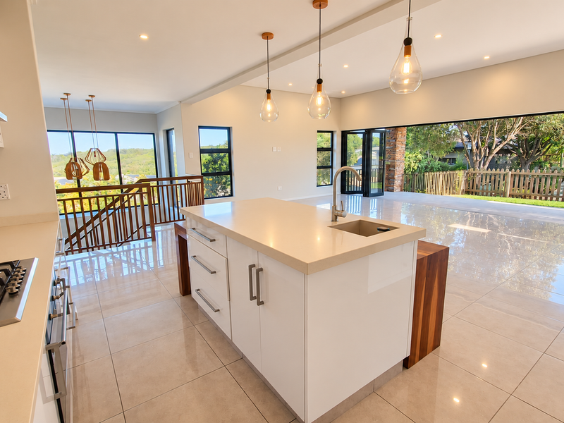 Modern open-plan kitchen and living area featuring a central island, stone countertops, gas hob, and large stacking doors opening to the outdoors.