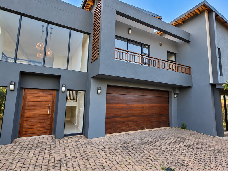 Modern double-story residence featuring a contemporary grey facade, timber garage and front door, and a spacious paved driveway.