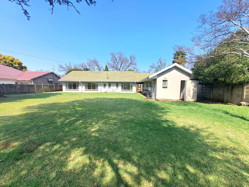 Rear view of the house featuring a large, well-maintained lawn and a tiled roof structure with perimeter boundary walls.