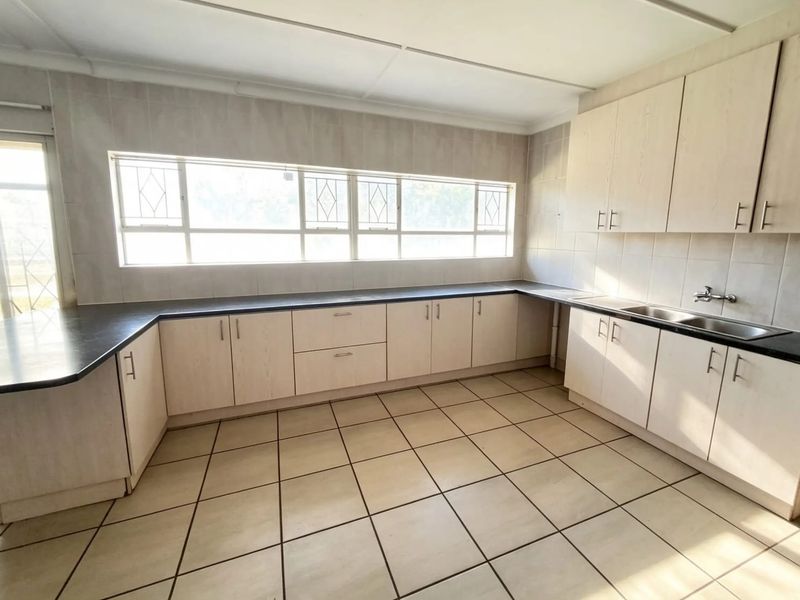 Spacious kitchen featuring light-toned cabinetry, dark countertops, double sink, and tiled flooring, offering a functional layout ready for modern updates.