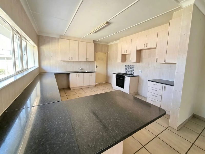 Spacious kitchen featuring ample built-in cabinetry, granite countertops, integrated oven and hob, and tiled flooring throughout.