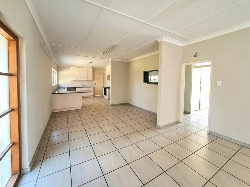 Spacious open-plan living and kitchen area featuring neutral tiled flooring, built-in cabinetry, and a functional layout ready for modern updates.