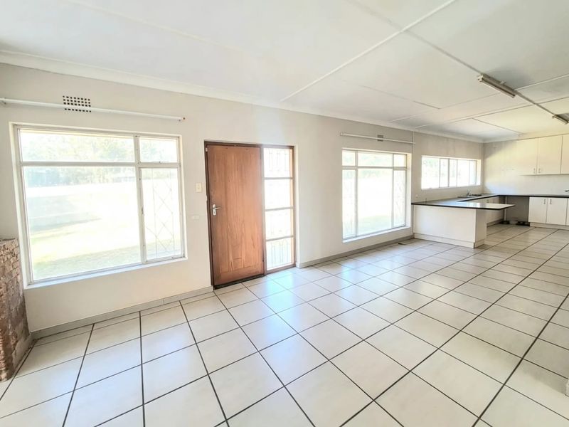 Spacious open-plan living and kitchen area featuring tiled flooring, a stone-clad fireplace, and ample natural light through large windows.