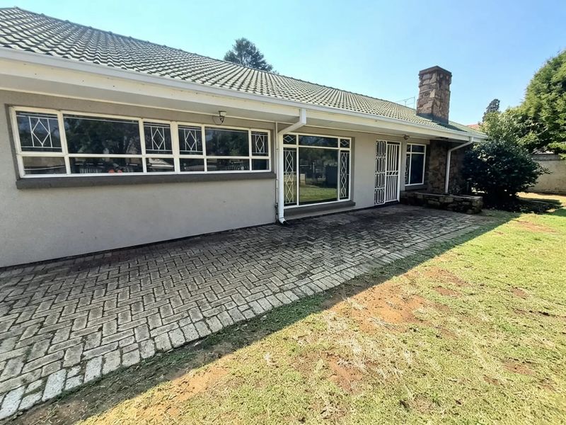 Rear exterior view of the house featuring a paved patio area, stone chimney, and large windows with security gates.