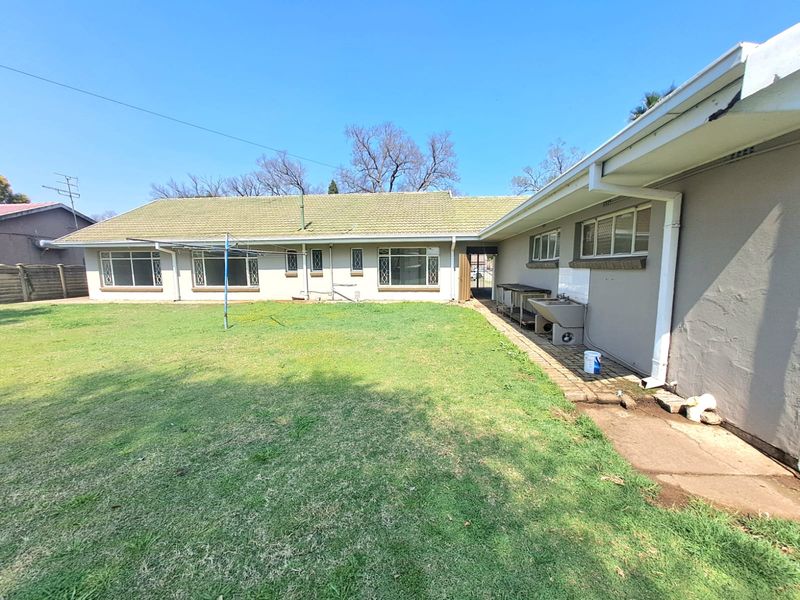 Rear view of the property featuring a large lawn, tiled roof, and an external utility sink area with paved walkway.
