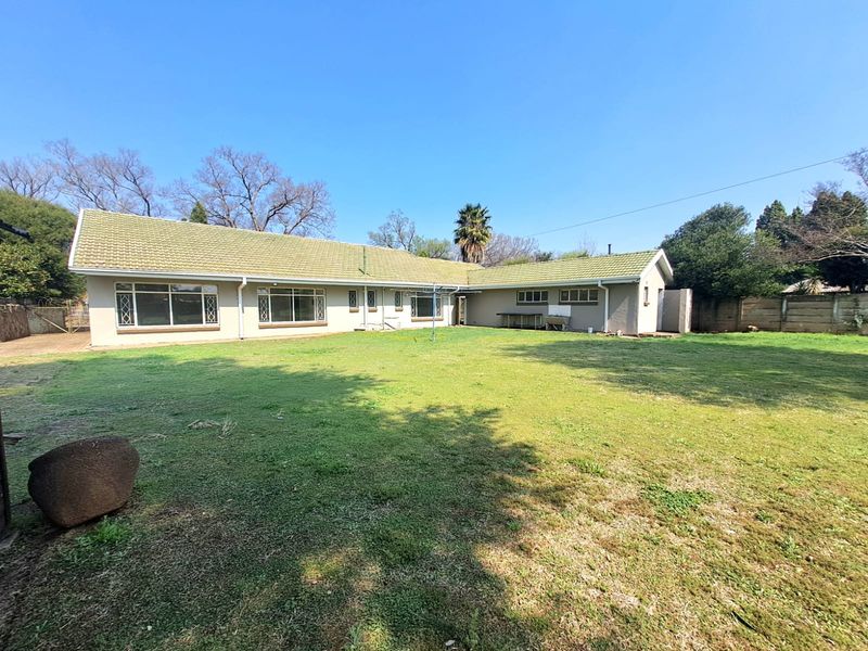 Spacious rear garden featuring a large lawn area and a single-story house with a tiled roof and aluminium window frames.