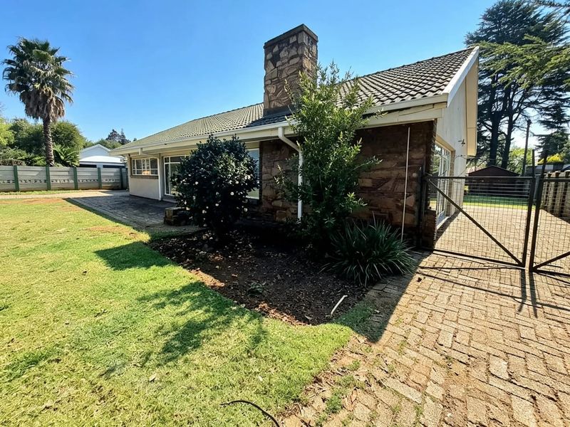 Rear view of the property featuring a stone chimney, tiled roof, paved driveway, and a well-maintained garden area with a metal gate.