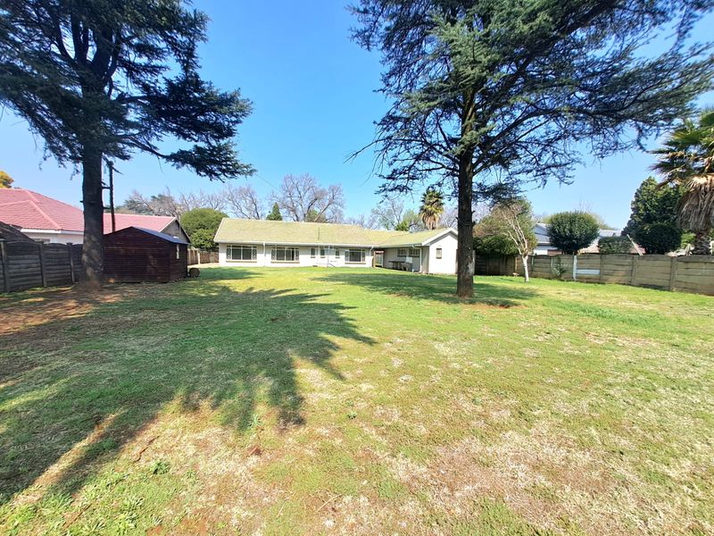 Spacious rear garden featuring a large lawn, mature trees, and a precast concrete boundary wall, providing a private outdoor area for the property.