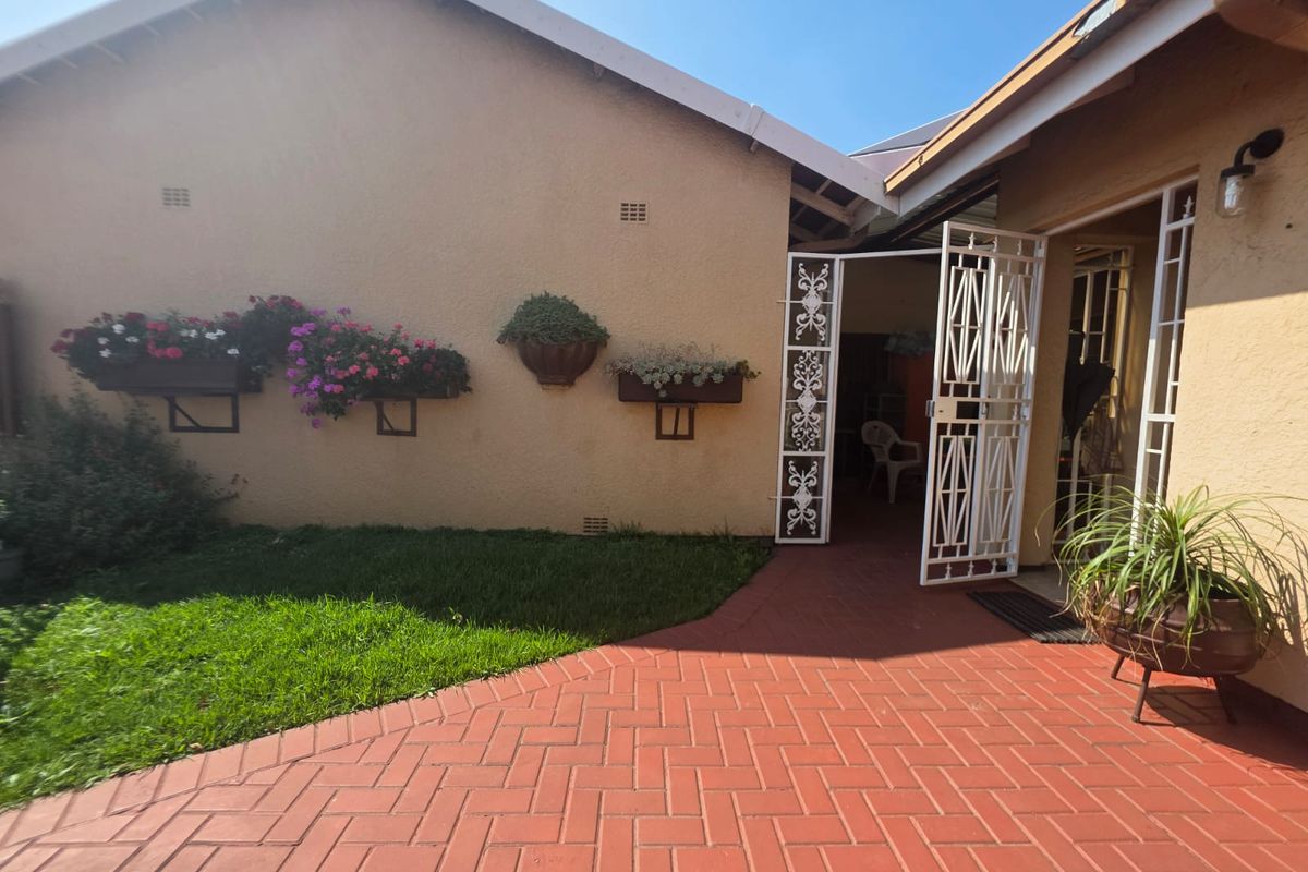 A well-maintained rear exterior area featuring a red brick paved patio, secure metal entrance gate, and wall-mounted planters against the townhouse facade.