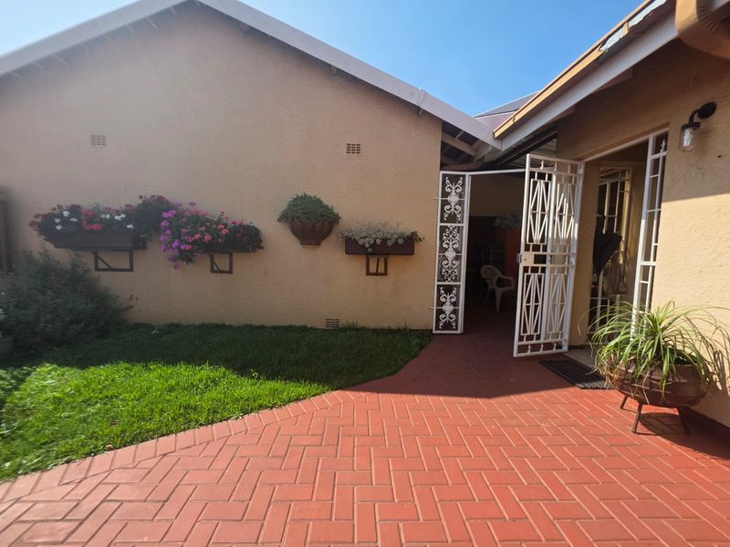 A well-maintained rear exterior area featuring a red brick paved patio, secure metal entrance gate, and wall-mounted planters against the townhouse facade.