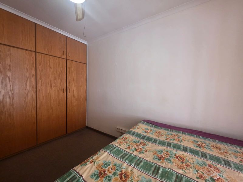 A bedroom featuring built-in wooden cupboards, carpeted flooring, and a ceiling fan, offering a functional space with potential for modernization.