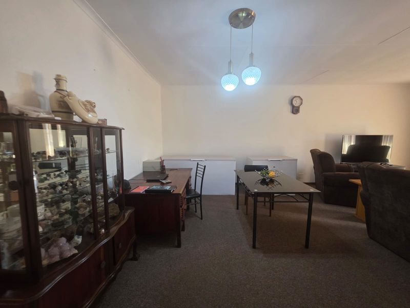 A spacious living area featuring carpeted flooring, coved ceilings, and a central pendant light fixture, offering a versatile layout for various furniture arrangements.