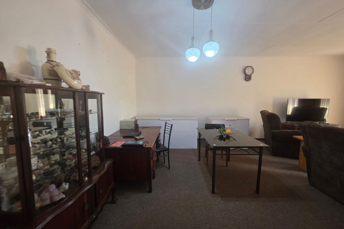 A spacious living area featuring carpeted flooring, coved ceilings, and a central pendant light fixture, offering a versatile layout for various furniture arrangements.