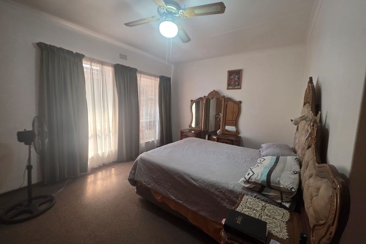 A standard bedroom featuring a ceiling fan and large windows with curtain tracks, offering a functional space with neutral wall finishes.