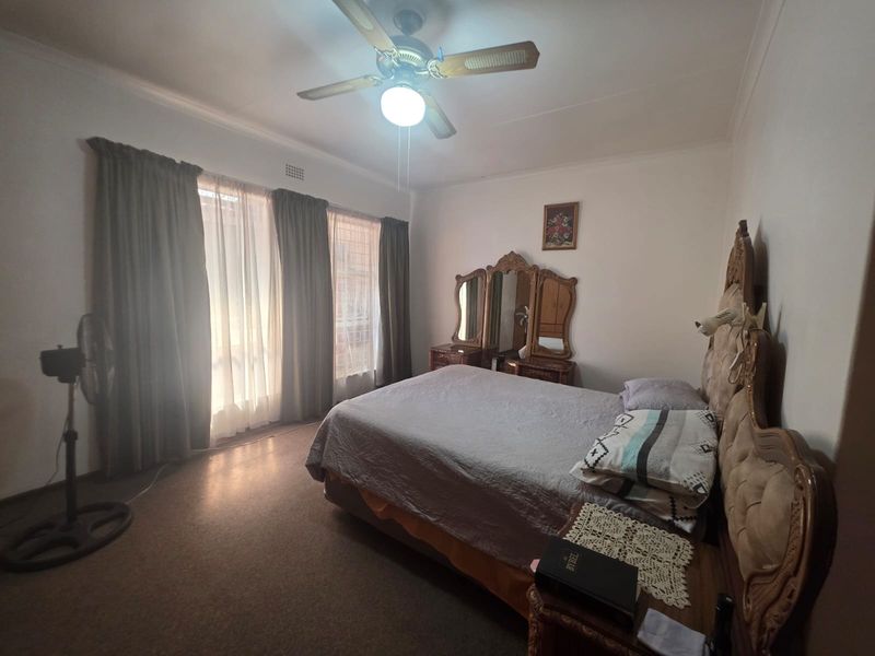 A standard bedroom featuring a ceiling fan and large windows with curtain tracks, offering a functional space with neutral wall finishes.