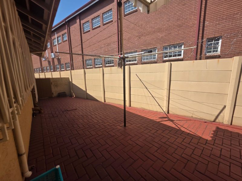 A private rear courtyard featuring red brick paving, a precast concrete boundary wall with security wire, and a fixed rotary clothesline.