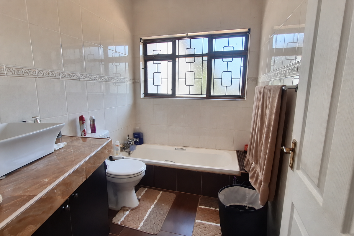 A functional bathroom featuring a vessel sink on a vanity cabinet, a bathtub, and tiled finishes throughout with security bars on the window.