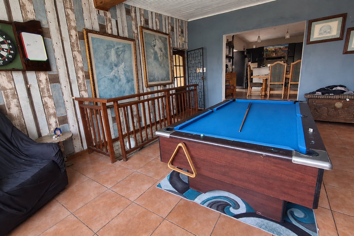 Spacious living area featuring tiled flooring, a wooden balustrade, and a beadboard ceiling, with an open-plan flow leading into the kitchen and dining space.