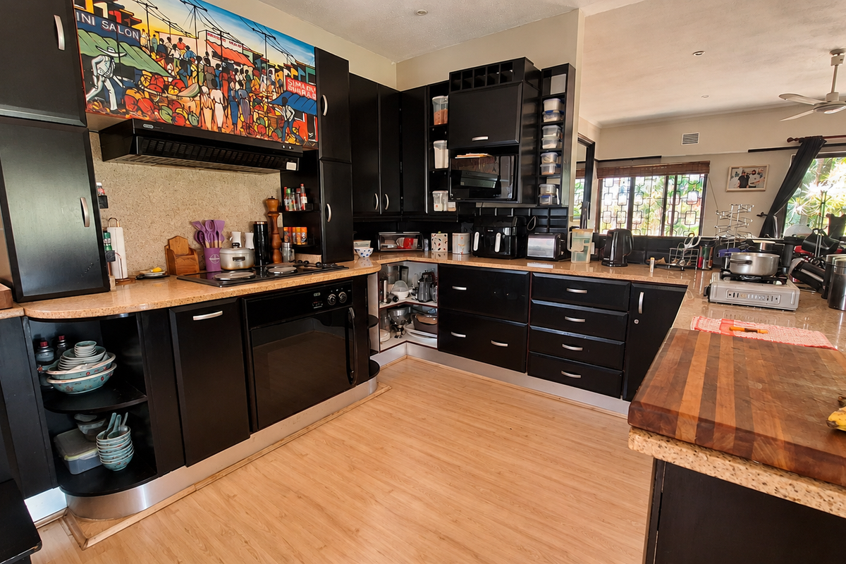 A well-equipped kitchen featuring dark cabinetry, stone countertops, built-in oven, and hob, with an open-plan layout flowing into the adjacent living area.