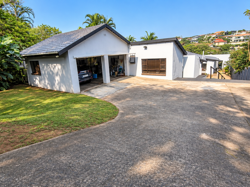 Front exterior view of the property featuring a double garage, concrete driveway, and established garden area.