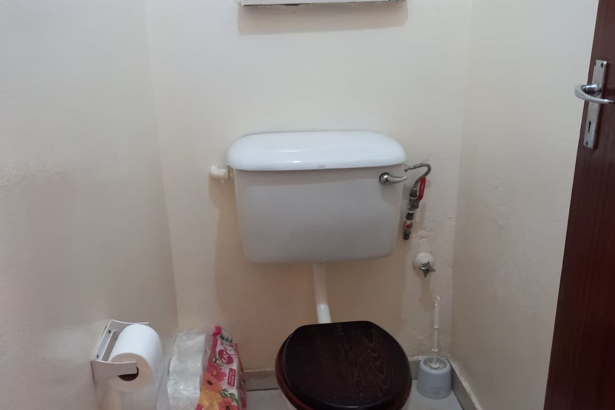 A compact bathroom featuring a standard toilet with a wooden seat and a recessed wall shelf for storage.