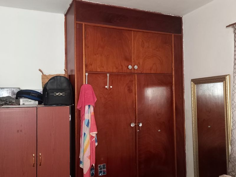 A bedroom featuring a large, dated built-in wooden wardrobe with overhead storage compartments.