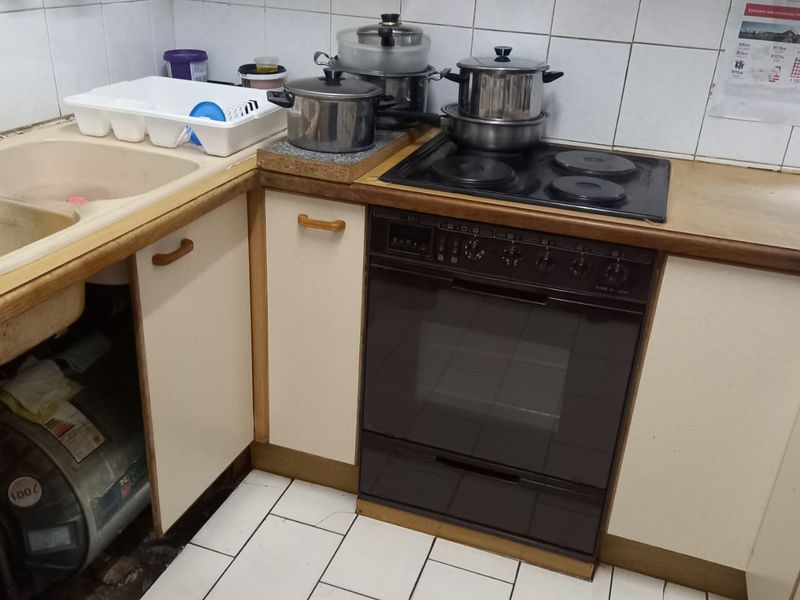 A dated kitchen featuring a built-in oven, electric hob, tiled backsplash, and laminate countertops, requiring cosmetic updates and repairs to cabinetry and flooring.