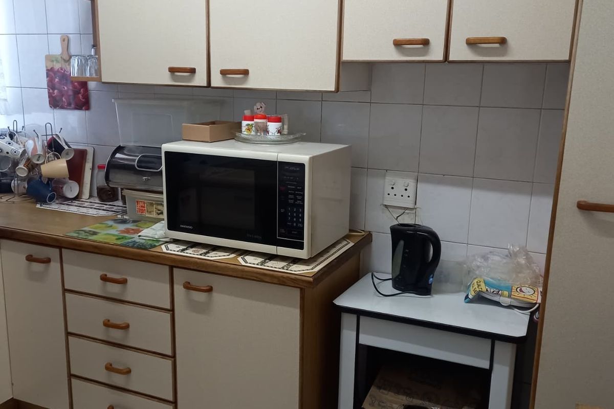 A compact kitchen featuring dated built-in cabinetry, tiled backsplash, and tiled flooring, offering a functional layout with potential for modern cosmetic updates.