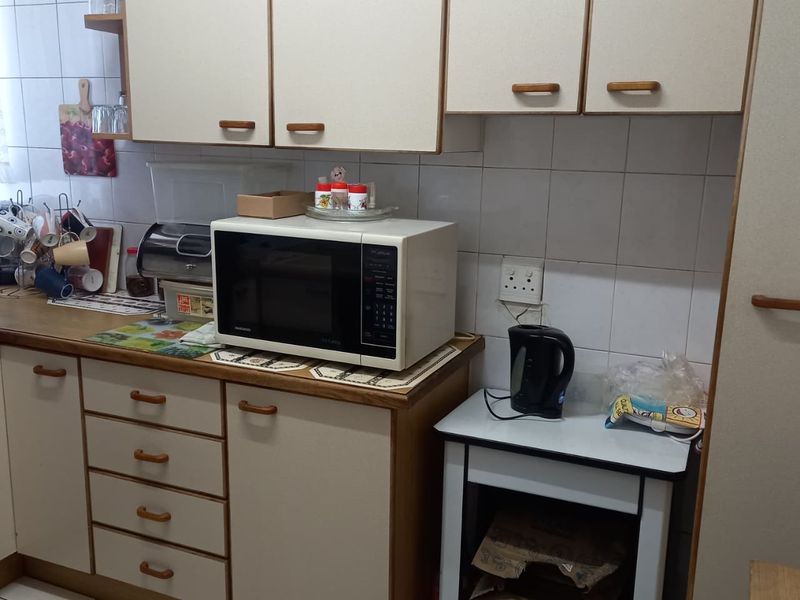 A compact kitchen featuring dated built-in cabinetry, tiled backsplash, and tiled flooring, offering a functional layout with potential for modern cosmetic updates.
