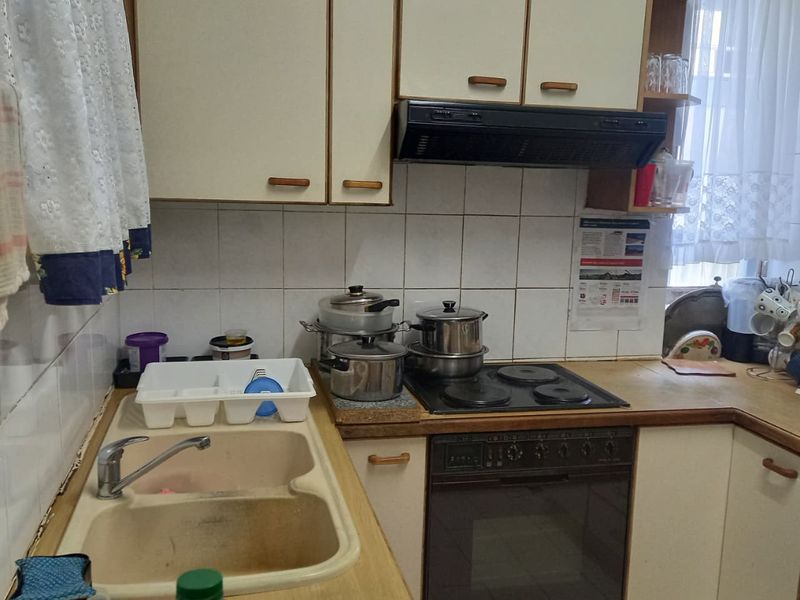 A functional kitchen featuring laminate countertops, a built-in oven with electric hob, extractor fan, and a double bowl sink with tiled splashback.