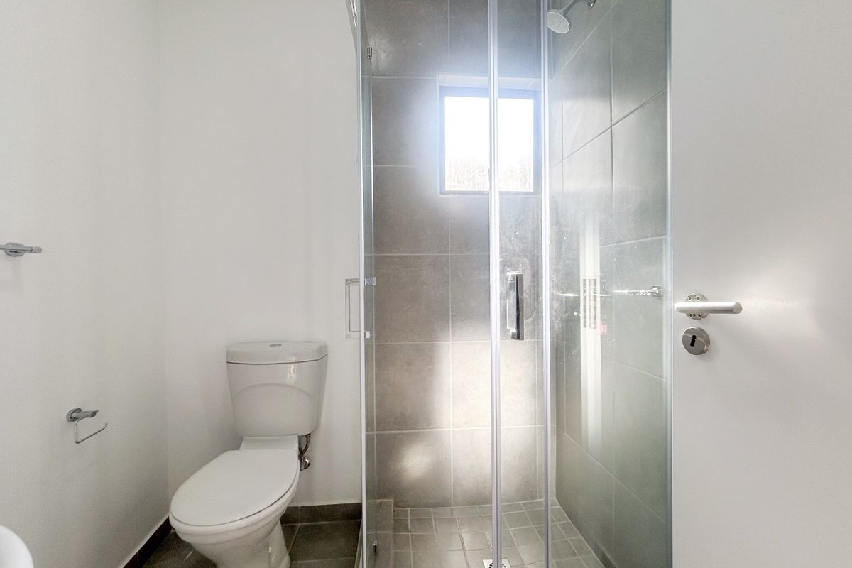 A clean, modern bathroom featuring a glass-enclosed shower with grey tiling and a standard toilet.