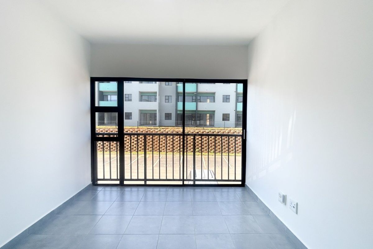 A bright, empty living area featuring neutral tiled flooring and a large sliding glass door that provides natural light and access to the exterior.