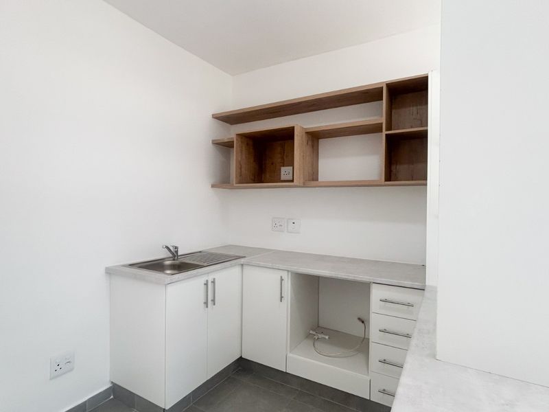 A clean and modern laundry area featuring white cabinetry, open wooden shelving, a stainless steel sink, and dedicated space for an appliance.
