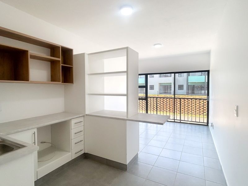 Modern open-plan kitchen and living area featuring tiled floors, built-in cabinetry, and a sliding door leading to a balcony with exterior views.