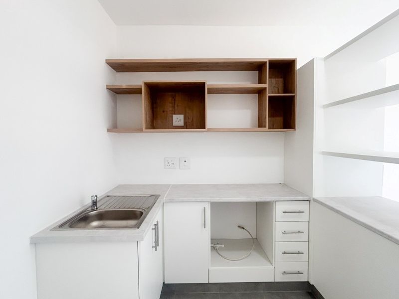 A clean, modern scullery featuring built-in cabinetry, open wooden shelving, a stainless steel sink, and dedicated plumbing connections for laundry or kitchen appliances.