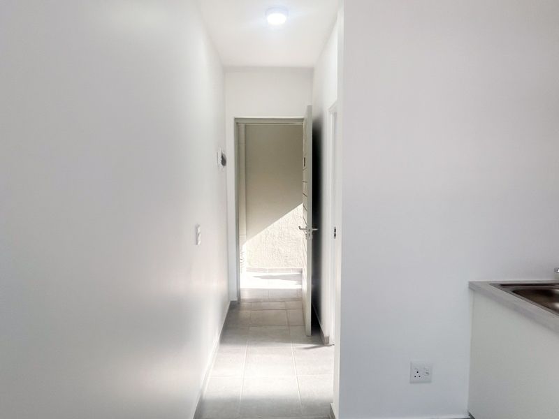 A clean, minimalist hallway featuring neutral tiled flooring, bright white walls, and a small integrated sink area.