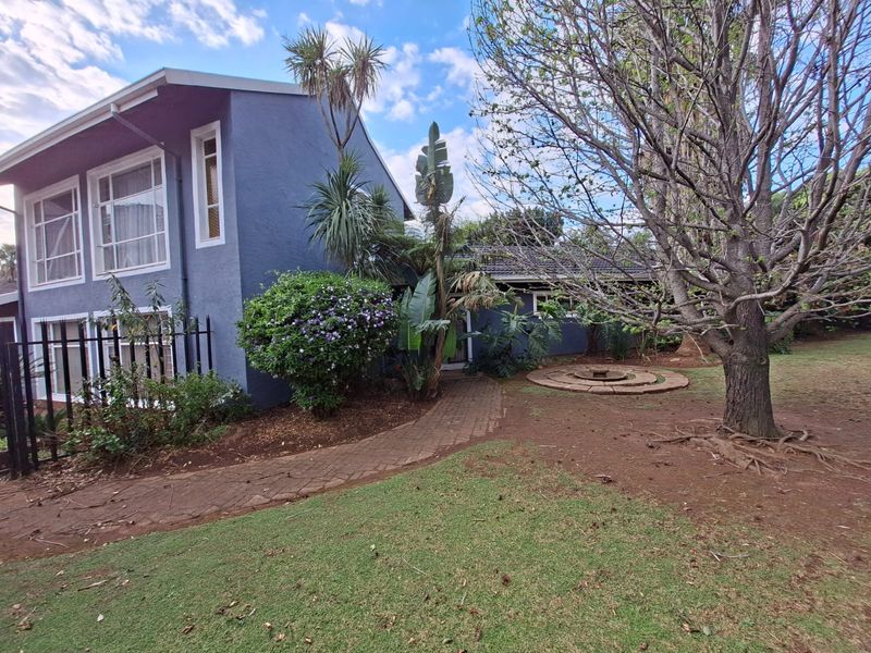 Rear view of the property featuring a brick pathway, established garden, and a stone circular feature set against the painted exterior walls.