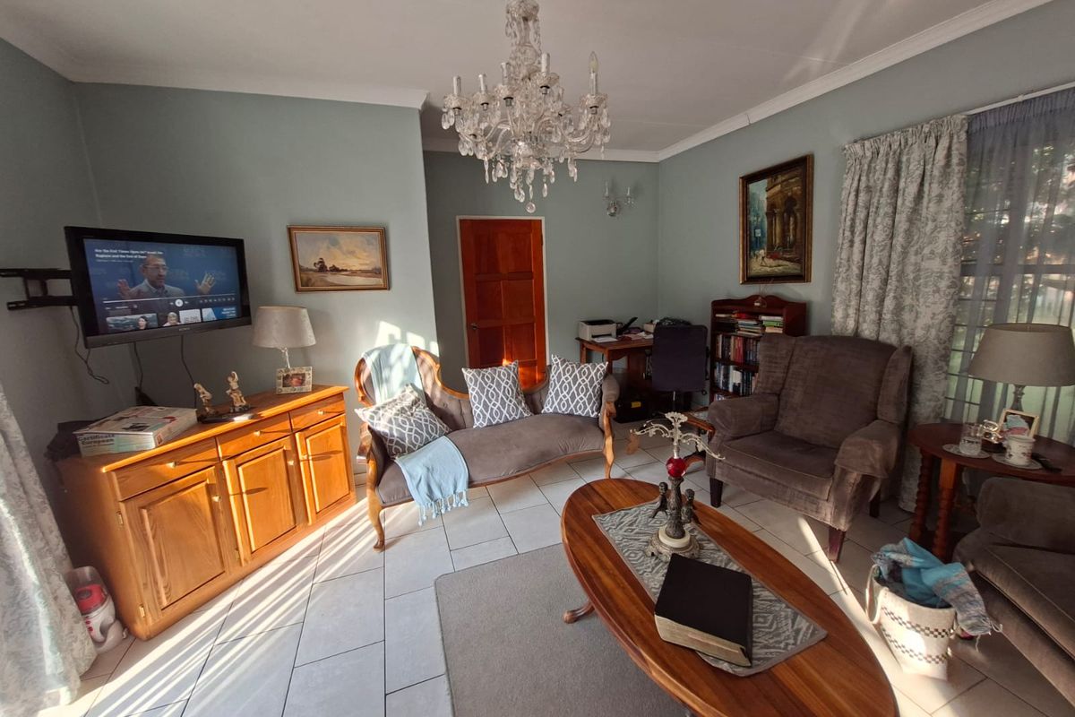 A comfortable living room featuring tiled flooring, a decorative ceiling rose, and a classic timber door, offering a functional and well-lit living space.