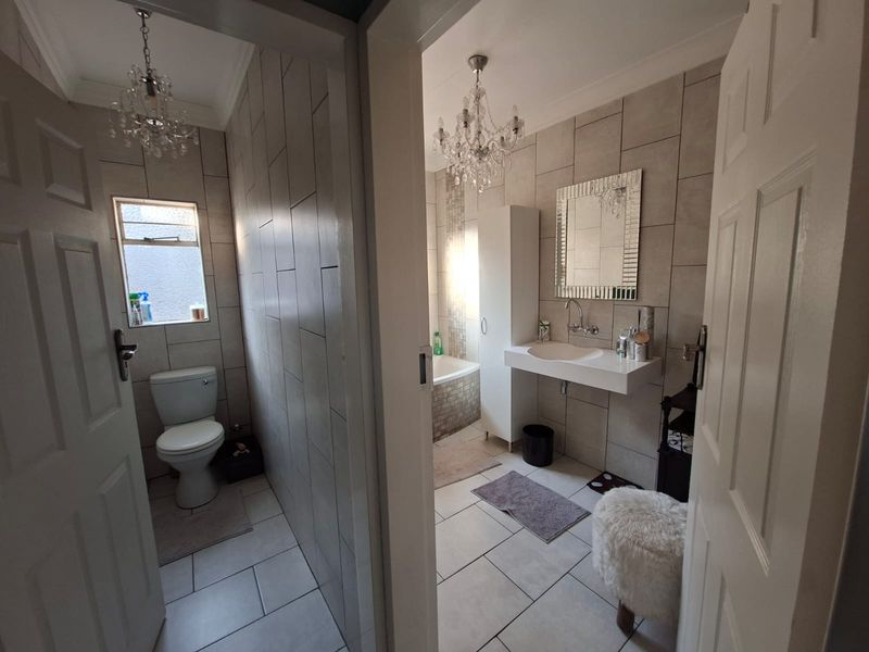 A well-maintained bathroom featuring tiled walls and flooring, a wall-mounted basin, a bathtub, and a separate toilet area with modern finishes.