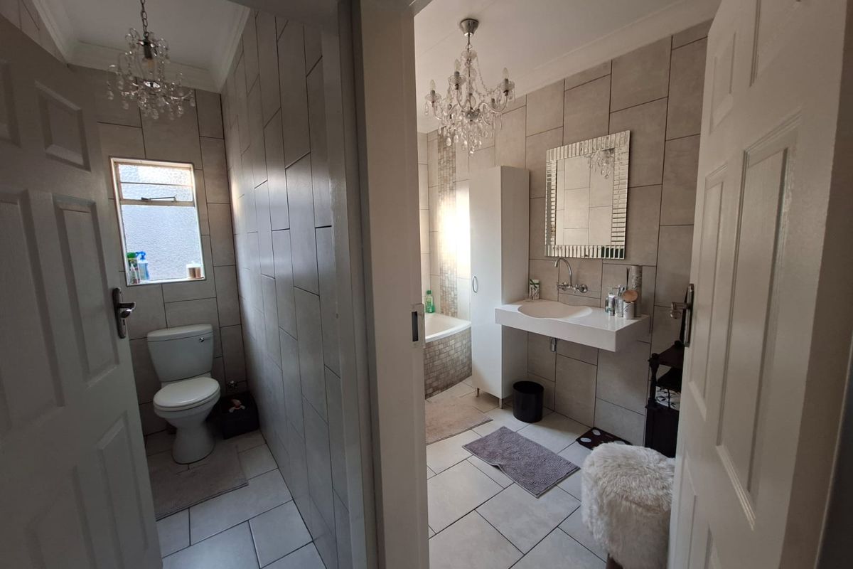A well-maintained bathroom featuring tiled walls and flooring, a wall-mounted basin, a bathtub, and a separate toilet area with modern finishes.